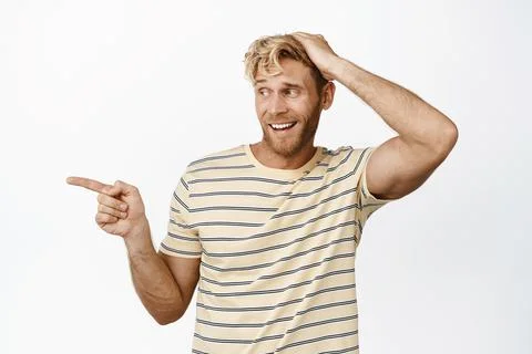 Portrait of smiling blond man, touching his head, pointing and looking left with Fotos Stock