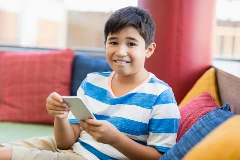 Portrait of smiling boy using mobile phone in library Stock Photos
