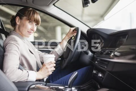 Portrait Of Smiling Businesswoman Driving Car With Coffee To Go In One Hand