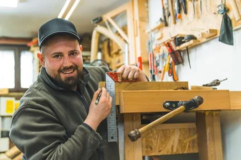 Portrait of a smiling carpenter using a setsquare to measure the wooden board Stock Photos