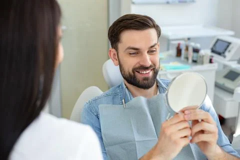 Portrait of smiling client looking at teeth in the mirror Stock Photos