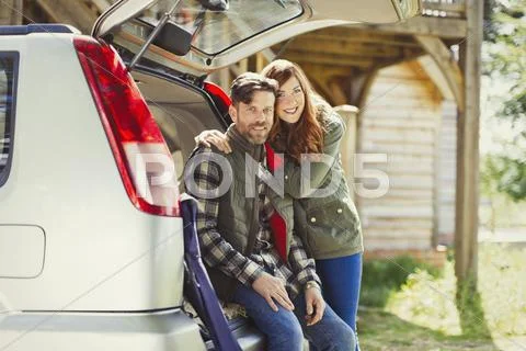 Portrait smiling couple at back of car outside cabin Stock Photos