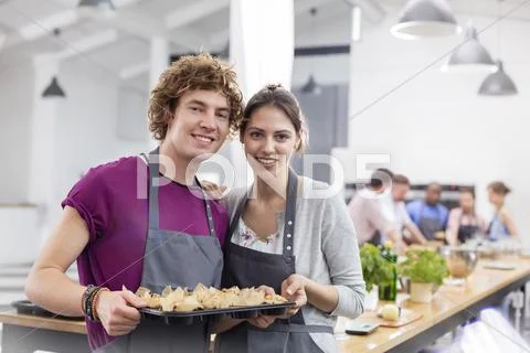 Portrait smiling couple with tray of food in cooking class kitchen Stock Photos