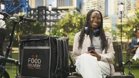 Portrait of smiling courier looking at the camera seated with smartphone Stock Photos