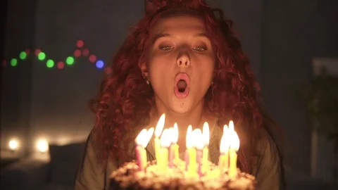 Portrait of a smiling curly red haired girl making a wish and blowing candles Stock Footage 119285860