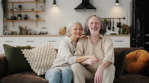 Portrait of smiling elderly 60s husband and wife sit relax on couch hugging Stock Footage 237706264