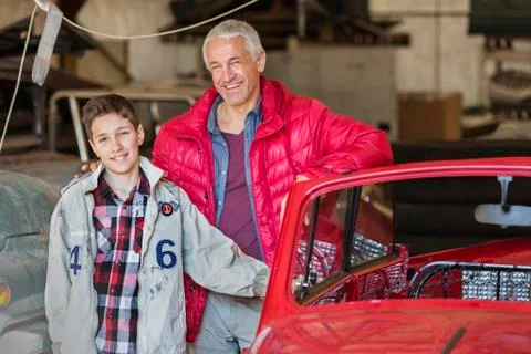 Portrait smiling father and son next to classic car in auto repair shop Stock Photos