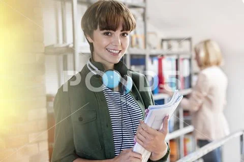 Portrait smiling female design professional with headphones holding paperwork in Stock Photos