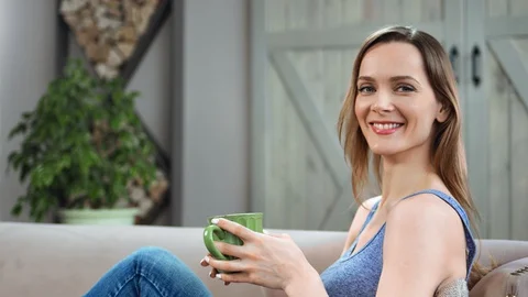 Portrait of smiling lady posing with mug at comfortable couch. Shot on RED Raven Stock-Footage 129947477