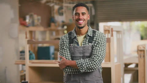 Portrait Of Smiling Male Apprentice Working As Carpenter In Furniture Workshop Stock Footage 242483755