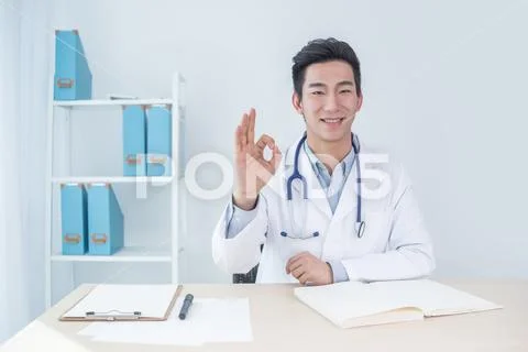 Portrait of a smiling male doctor gesturing okay sign at medical office Stock Photos