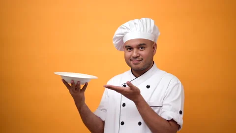 Portrait of smiling man chef showing white empty plate on isolated yellow. Stock Footage 172283989