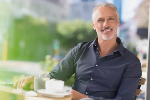 Portrait smiling man drinking coffee at urban sidewalk cafe Stock Photos