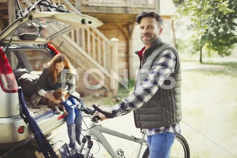 Portrait smiling man with mountain bike near car behind cabin Stock Photos