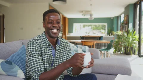 Portrait Of Smiling Man Relaxing On Sofa In Lounge Dining Room At Home Holding Stock-Footage 239657703