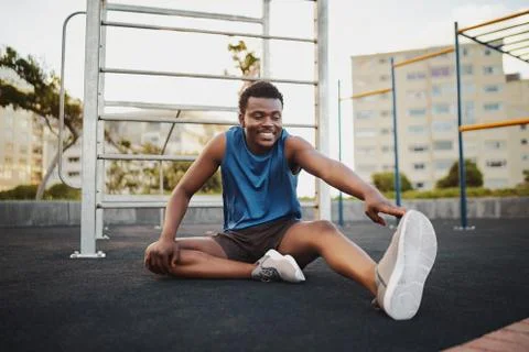 Portrait of a smiling man runner sitting on outdoor gym park stretching legs Stock Photos