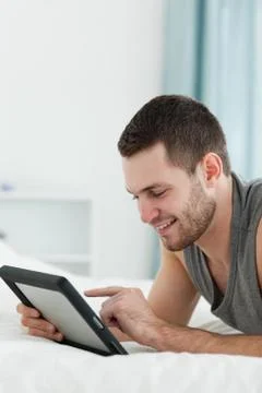 Portrait of a smiling man using a tablet computer while lying on his belly Foto stock