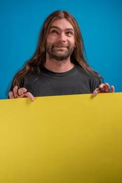 Portrait of smiling man while looking up and holding a yellow advertise banner Stock Photos