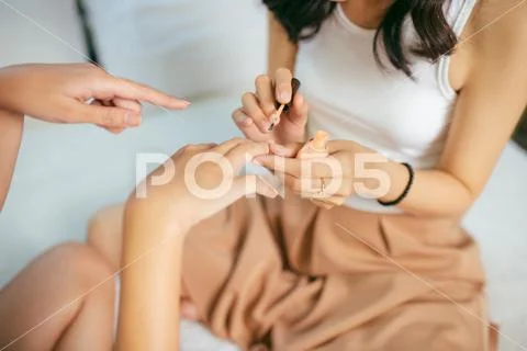 Portrait of a smiling pretty young woman painting friend's nails over white b Stock Photos