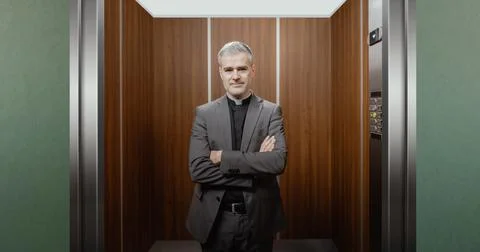 Portrait of a smiling priest standing in an elevator Stock Photos