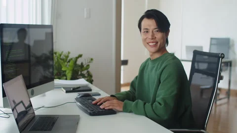 Portrait of Smiling Programmer Typing Code on Keyboard in front of Monitor Video stock 256974907