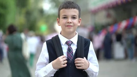 Portrait of smiling schoolboy in uniform and backpack standing near school 库存影片 344312864