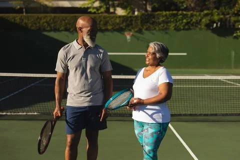 Portrait of smiling senior african american couple with tennis rackets on tennis Stock Photos