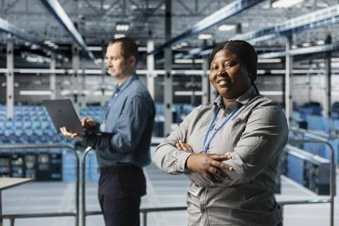 Portrait of smiling server room engineer next to coworker troubleshooting errors Stock Photos