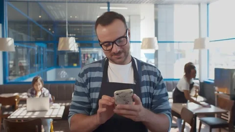 Portrait of smiling waiter in apron using mobile phone in restaurant Stock Footage 134542871