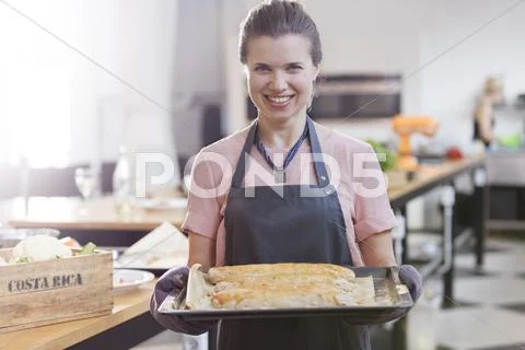 Portrait smiling woman holding tray of food in cooking class kitchen Stock Photos