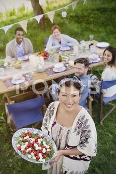 Portrait smiling woman serving Caprese salad to friends at garden party table Stock Photos
