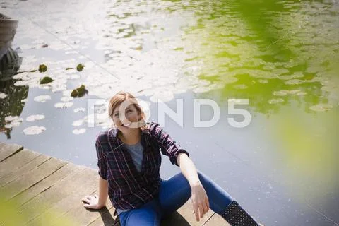 Portrait smiling woman sitting on sunny lakeside dock Stock Photos