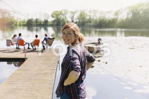 Portrait smiling woman at sunny lakeside dock Stock Photos