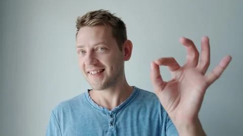 Portrait of a smiling young Caucasian man showing ok gesture while standing and Stock Footage 252132417