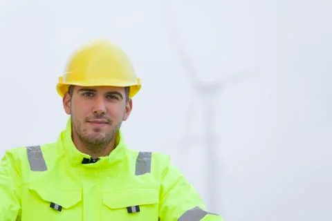 Portrait of smiling young engineer in front of blurred wind turbines Фото