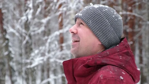 Portrait of a smiling young man looking up at the falling snow in a winter park Stock Footage 166149594
