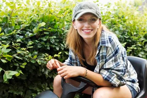 Portrait of a smiling young woman sitting on a lawn-mower Stock Photos