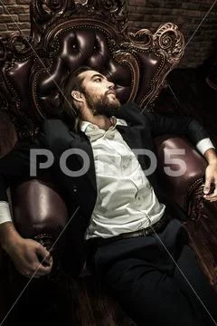 Portrait of a stylish handsome man on a vintage armchair. Fashion shot. Men's Stock Photos