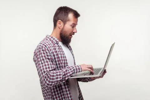 Portrait of surprised computer user, bearded man standing with laptop and typ Stock-Fotos