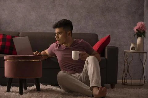 Portrait of a surprised young man using laptop in living room Stock Photos