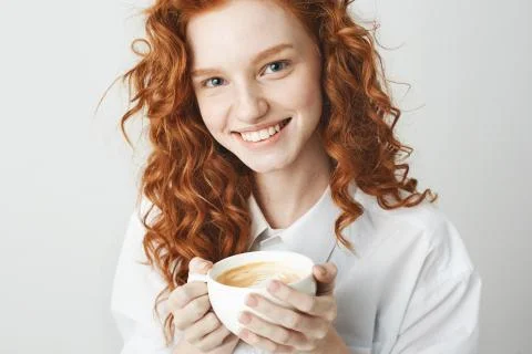 Portrait of tender redhead girl with freckles smiling holding cup looking at Stock Photos