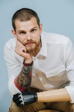 Portrait of a thoughtful man with prosthetic bionic arm over blue background Stock Photos