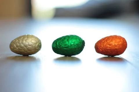 A portrait of three chocolat easter eggs in colorful tin foil lying on the fl Stock Photos