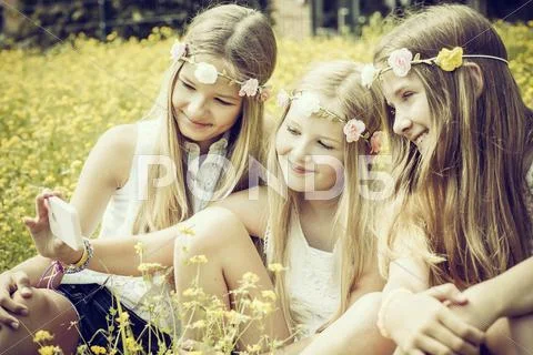 Portrait of three girls wearing floral wreaths taking a selfie on a flower Stock Photos