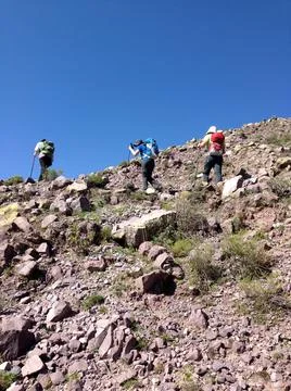 Portrait of three hikers climbing rocky hillside with blue sky Stock Photos