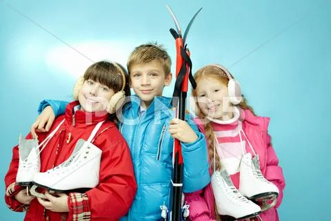 Portrait of three little children with skates and skis looking at camera and smi Stock Photos