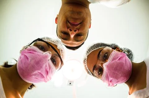 Portrait of three surgeons at work, operating in uniform, looking at the camera. Stock Photos