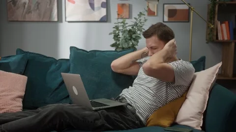 Portrait of tired man sitting at sofa and working remote on computer desktop in Stock Footage 150436741
