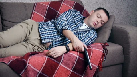Portrait of tired man sleeping on couch alone holding TV remote control Video stock 119535046