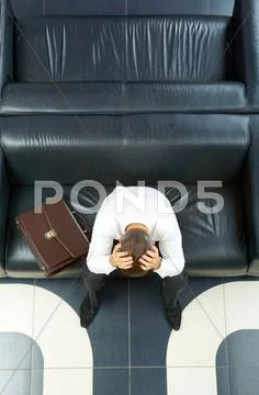 Portrait of troubled businessman touching head while sitting on sofa Stock Photos